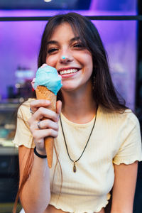 Crop cheerful young female in pendant and earrings with delicious gelato in waffle cone looking at camera on street