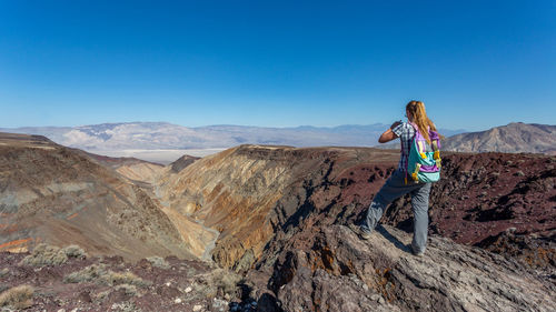 Woman on rock by mountains against clear blue sky
