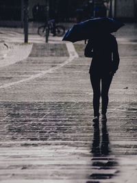 Full length of person carrying umbrella walking on wet cobbled street during rainy season