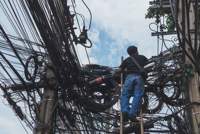 Low angle view of man working on electricity pylon against sky