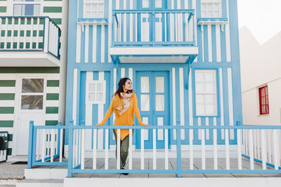 Happy woman standing in front of colorful houses.promenade of costa nova, aveiro, portugal