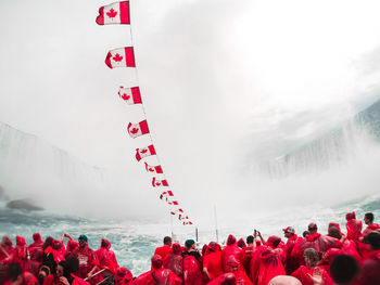 Canadian flags hanging over tourists against niagara falls