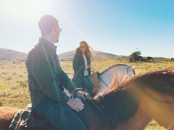 Couple riding horses on land against clear sky during sunny day
