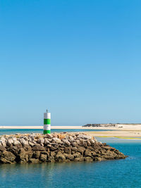 Lighthouse by sea against clear blue sky