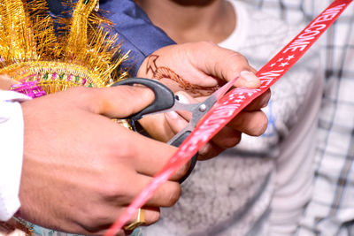 Midsection of groom cutting ribbon during wedding ceremony