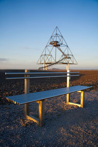 Empty bench on beach against clear sky