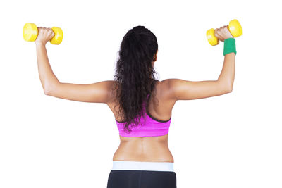 Rear view of woman exercising with dumbbells against white background