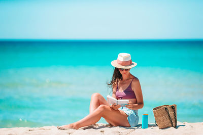 Woman wearing hat while sitting on beach against sky