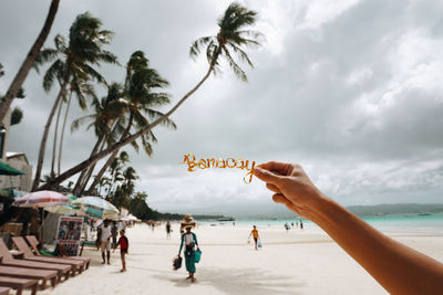 Cropped hand holding text at beach against cloudy sky