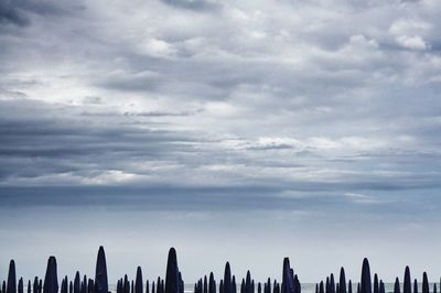 Fence at beach against cloudy sky