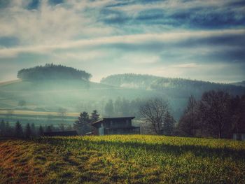 Barn on grassy field against sky during foggy weather