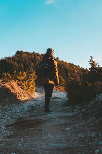 Rear view of woman standing on footpath against clear sky