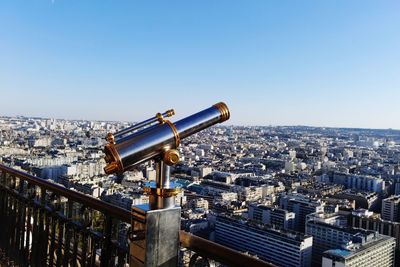 Hand-held telescope at observation point with city in background against clear sky