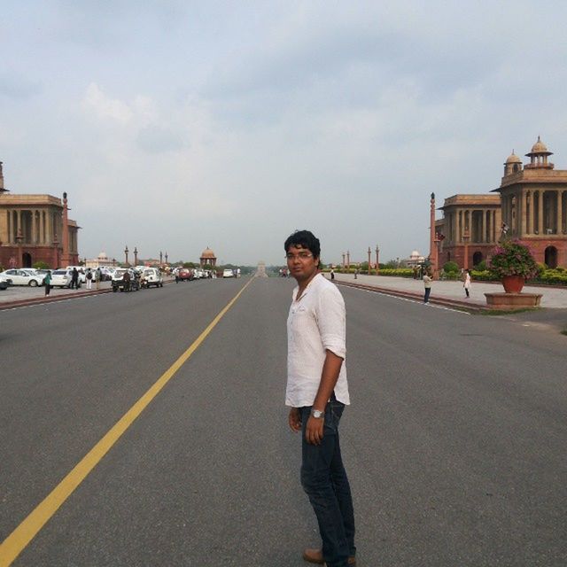 PORTRAIT OF YOUNG MAN STANDING ON ROAD AGAINST BUILDINGS