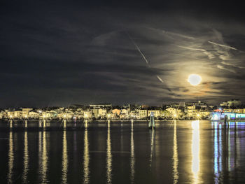 Illuminated city by sea against sky at night