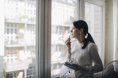 Creative female business professional talking through earphones while standing by window in office