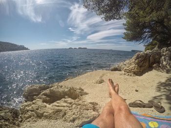 Low section of man relaxing on beach against sky