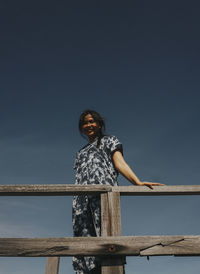 Portrait of young woman standing on railing against clear sky