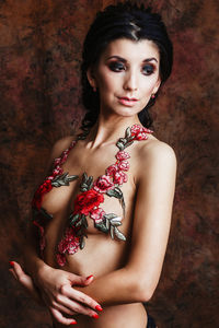 Shirtless young woman with floral decoration standing against wall