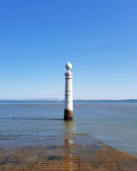 Lighthouse by sea against clear blue sky