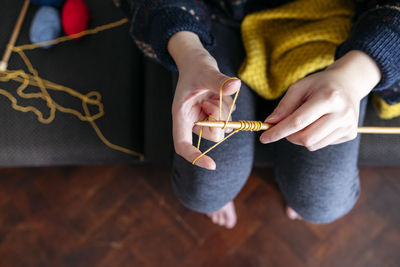 Woman knitting wool on sofa at home