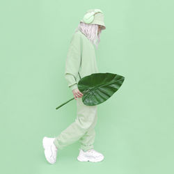 Side view of woman holding leaf standing over colored background