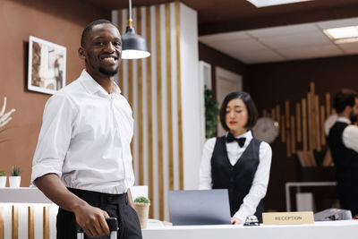 Portrait of young woman using mobile phone while standing in office