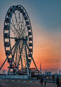 People at amusement park against sky during sunset