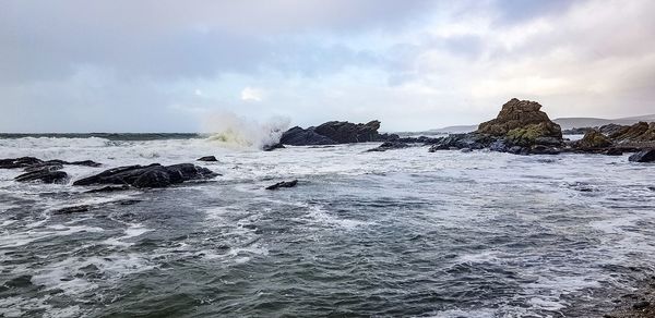 Sea waves splashing on rocks against sky