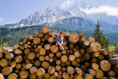 Woman sitting on the stack of the tree logs