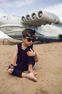 Rocker boy a child in black clothes stands against the background of an abandoned plane on the beach