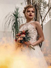 Low angle view of bride holding bouquet against trees