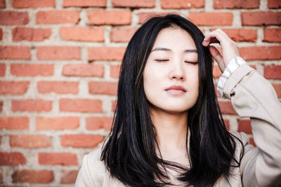 Relaxed beautiful chinese business woman standing over bricks wall background with eyes closed