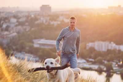 Man playing with dog on field against sky during sunset