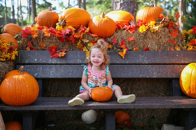 Portrait of smiling boy with pumpkins against orange autumn leaves