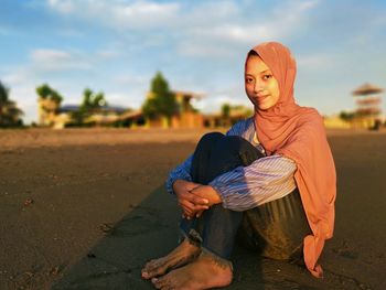 Young woman sitting on land against sky