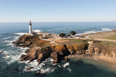 Lighthouse by sea against clear sky