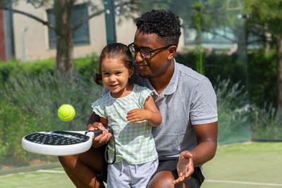 Black father teaching daughter to play paddle tennis
