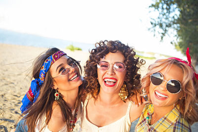 Cheerful female friends wearing sunglasses at beach against clear sky