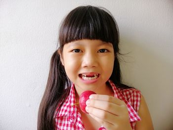 Portrait of cute girl holding fruit sitting against wall