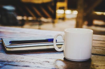 Close-up of coffee cup with diary and pen on wooden table