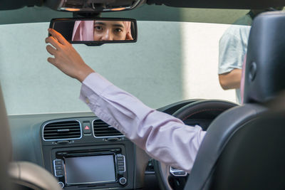 Young woman reflecting on rear-view mirror in car