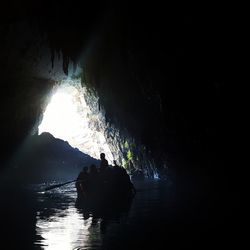 Silhouette people in cave against sky