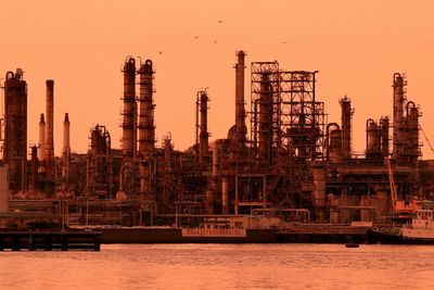 Factory by sea against sky at sunset