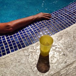 High angle view of drinking glass by person in swimming pool