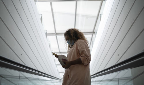 Young woman text messaging on smart phone while wearing protective face mask