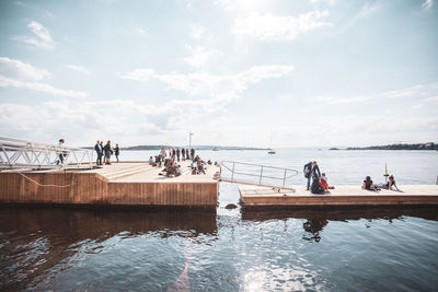 People on pier by sea against sky