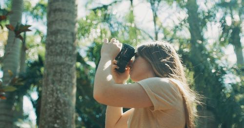 Midsection of woman holding camera while standing by tree