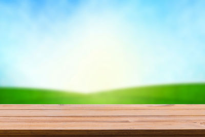 Wooden bench by field against sky