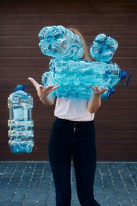 Young woman throwing out empty used plastic water bottles into trash bin. collecting plastic waste